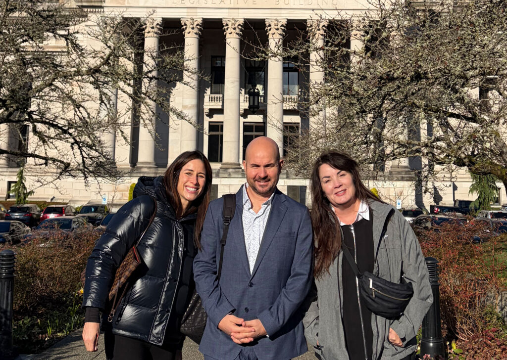 Three adults stand in front of an ornate capital building outside.