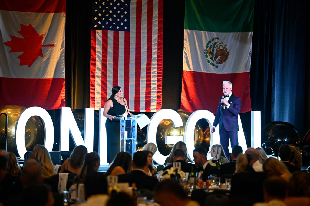 Room full of Gala attendees listening to event MC and auctioneer fundraising.