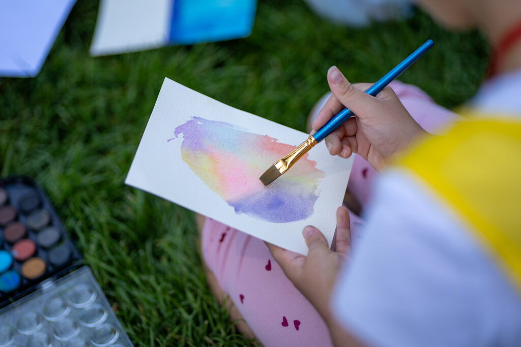Club kid painting with watercolor on a piece of paper.